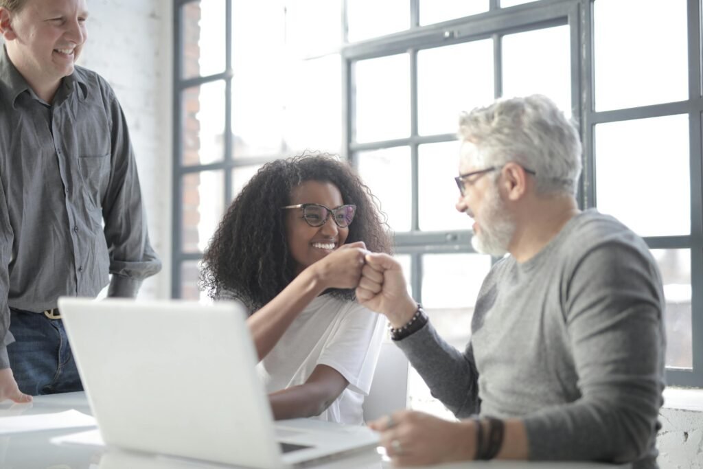 A man and woman fist bump each other while working at a laptop.